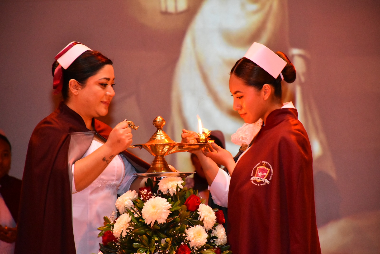 Ceremonia de la lámpara: una egresada enciende su lámpara de la mano de una maestra frente a la generación.