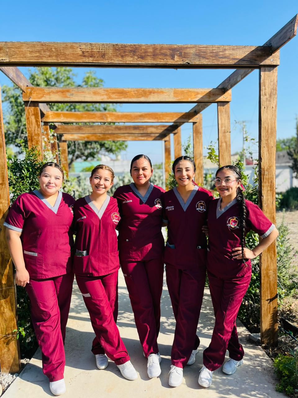 Estudiantes de la escuela en uniforme guinda, reunidas bajo una pérgola en el campus.
